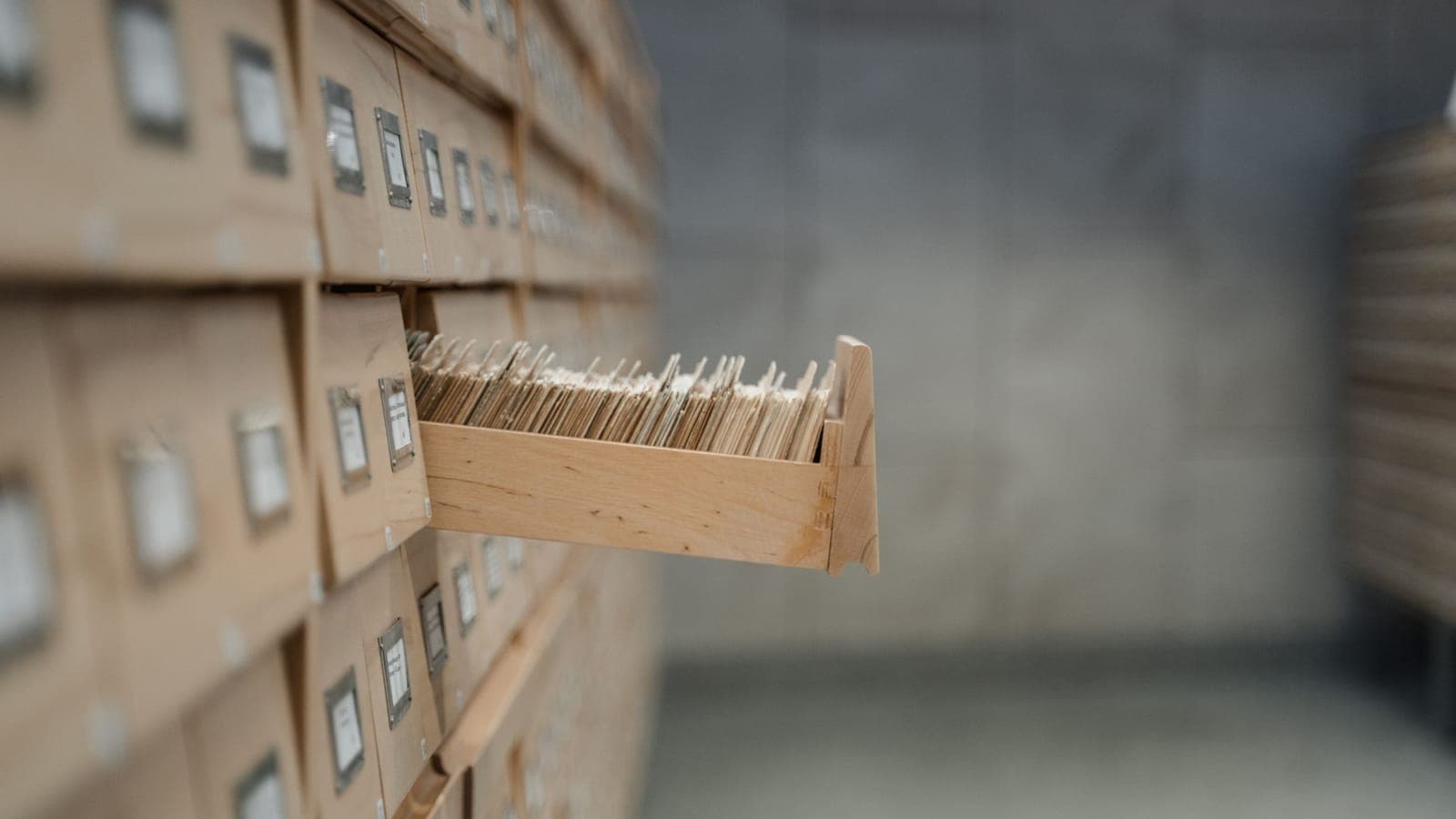 An open drawer in a wooden library card catalogue, packed with index cards.