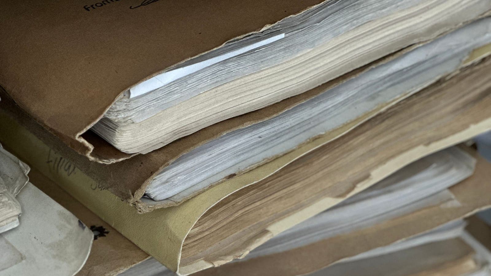 A stack of worn paper files with frayed edges, tied and archived.