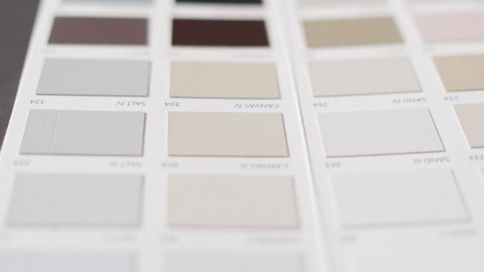 A fan of muted paint swatch cards in greys, sands and clays.