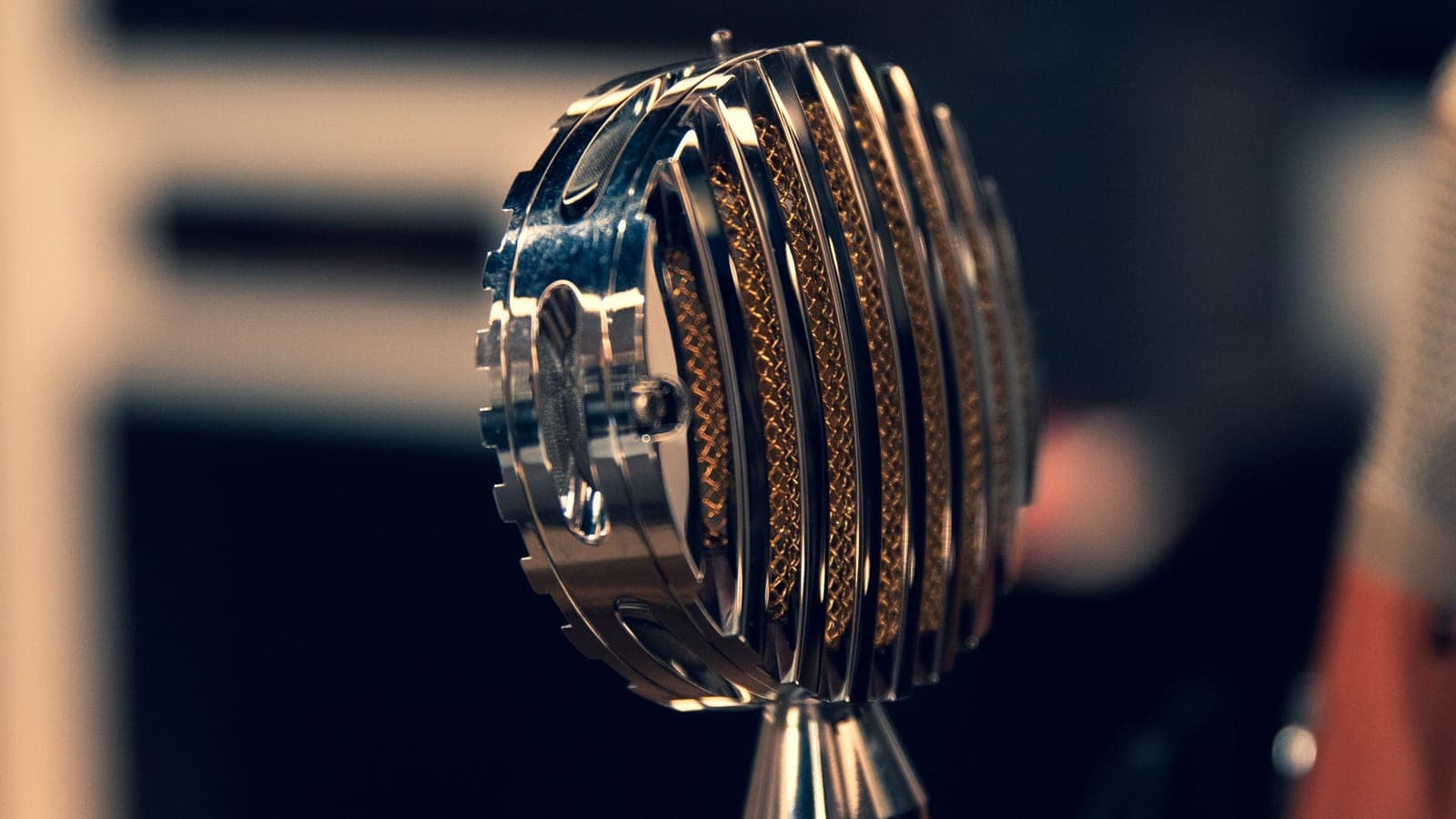 A chrome vintage condenser microphone in a darkened studio.